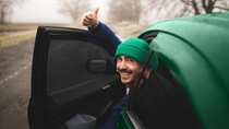 Man with green cap looking out of the car and holding his thumb up
