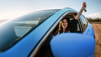 Woman in a blue car holding her arm up out of the window