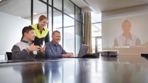 Three employees talking to a colleague on a screen in a virtual meeting Three employees talking to a colleague on a screen in a virtual meeting