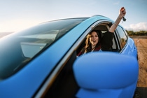 Woman in a blue car holding her arm up out of the window