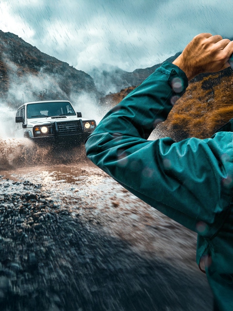 Person with rain jacket looks at a car driving through a puddle