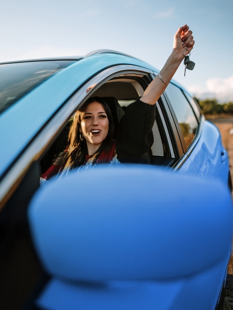 Woman in a blue car holding her arm up out of the window