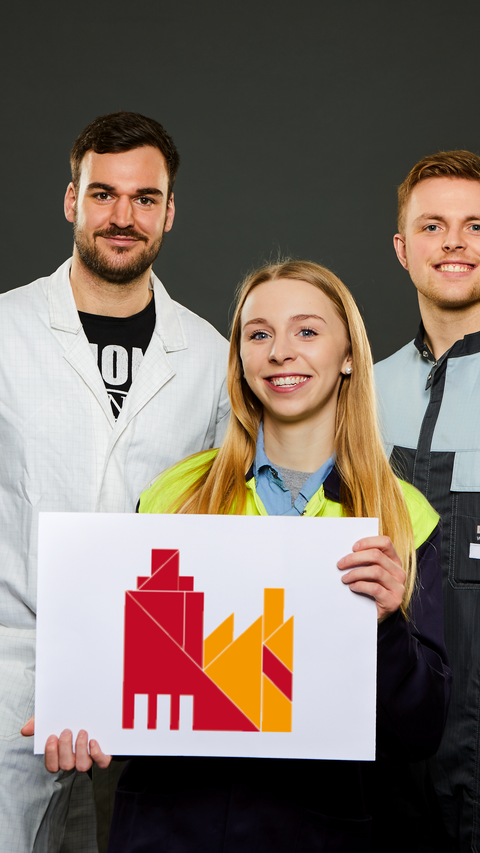 3 Azubis in Arbeitskleidung halten das Key Visual der BASF Würzburg 3 Azubis in Arbeitskleidung halten das Key Visual der BASF Würzburg